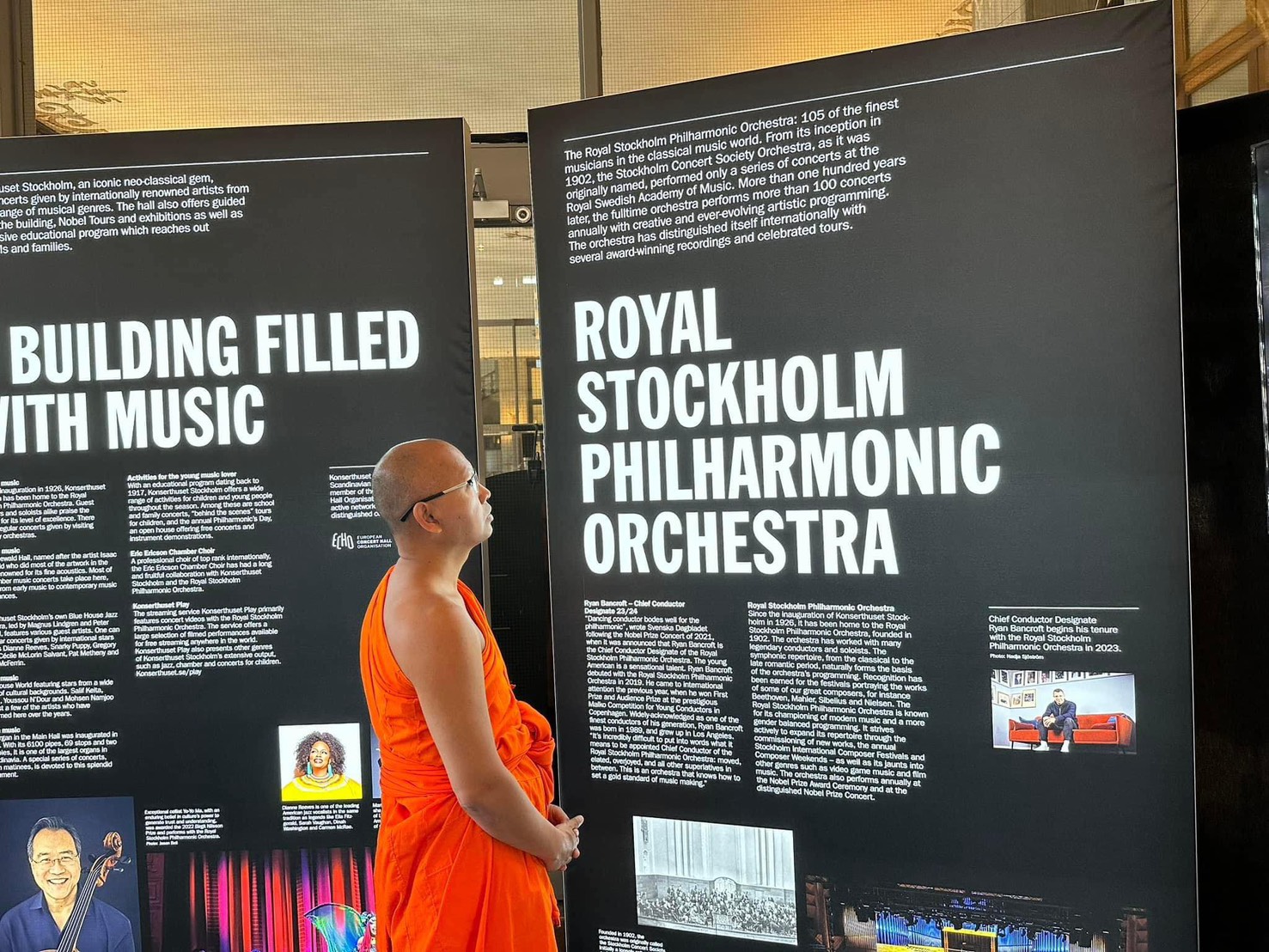 Guest in orange robes viewing exhibition boards inside Stockholm Concert Hall